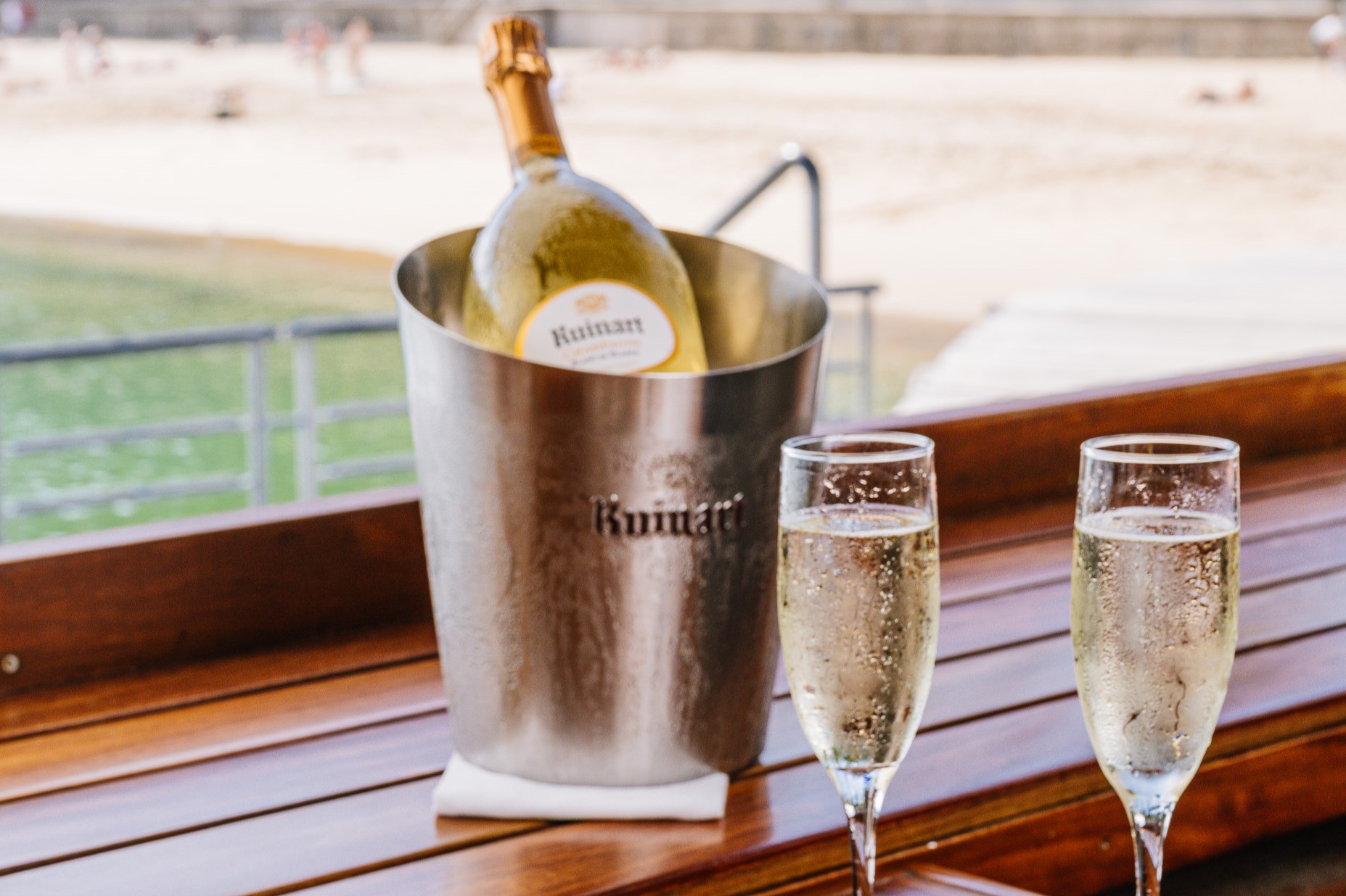 A bottle of champagne on ice with two filled flutes beside a window overlooking the beach